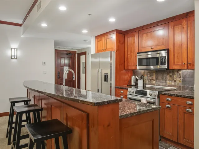 Kitchen with stainless steel appliances, brown cabinetry, dark stone countertops, a breakfast bar area, and recessed lighting