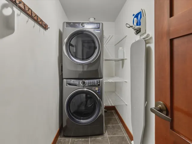 Laundry room featuring stacked washing machine and dryer and dark tile patterned floors