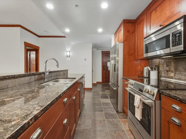 Kitchen featuring appliances with stainless steel finishes, dark stone counters, tasteful backsplash, brown cabinetry, and recessed lighting