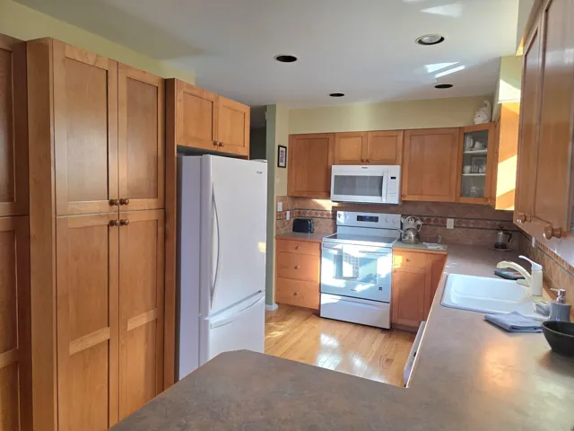 Kitchen featuring white appliances, light wood-style flooring, glass insert cabinets, decorative backsplash, and dark countertops
