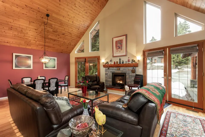 Living room featuring light wood finished floors, a stone fireplace, a vaulted wood ceiling, and french doors