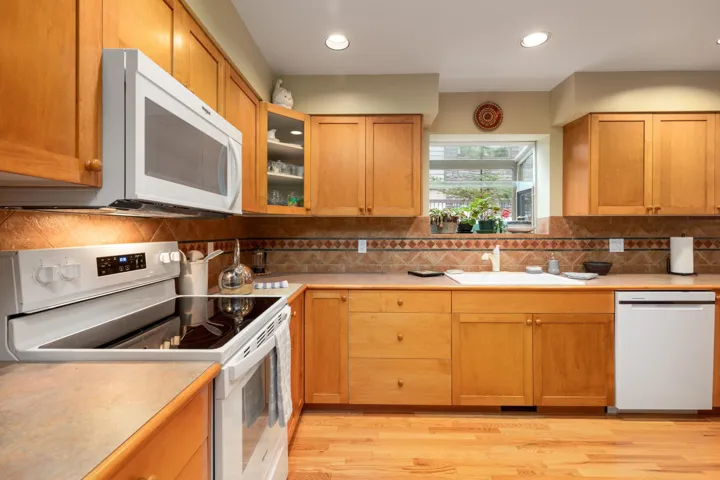 Kitchen featuring white appliances, light countertops, glass insert cabinets, light wood-type flooring, and recessed lighting