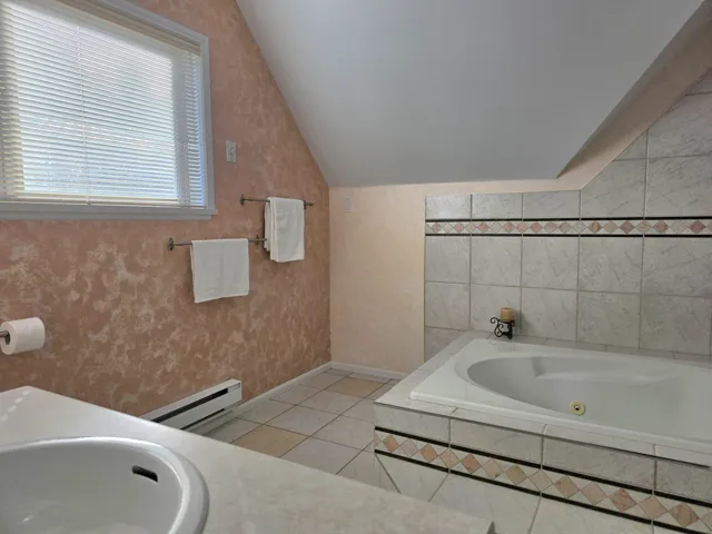Second Floor Semi Primary Full Bathroom reverse view with vanity, baseboard heating, lofted ceiling, a whirlpool tub, and light tile patterned floors