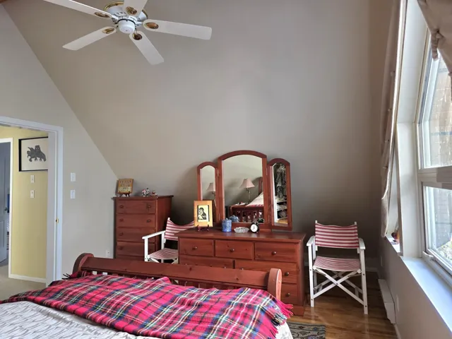 Primary Bedroom featuring ceiling fan, a baseboard radiator, wood finished floors, and multiple windows