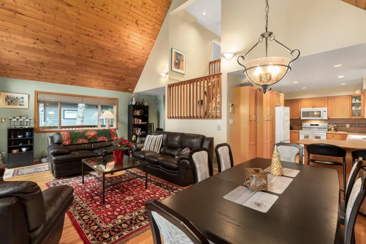 Living room featuring light wood-type flooring, suspended lighting, and a vaulted wood ceiling