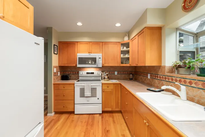 Kitchen with white appliances, light countertops, light wood-style flooring, decorative backsplash, and recessed lighting
