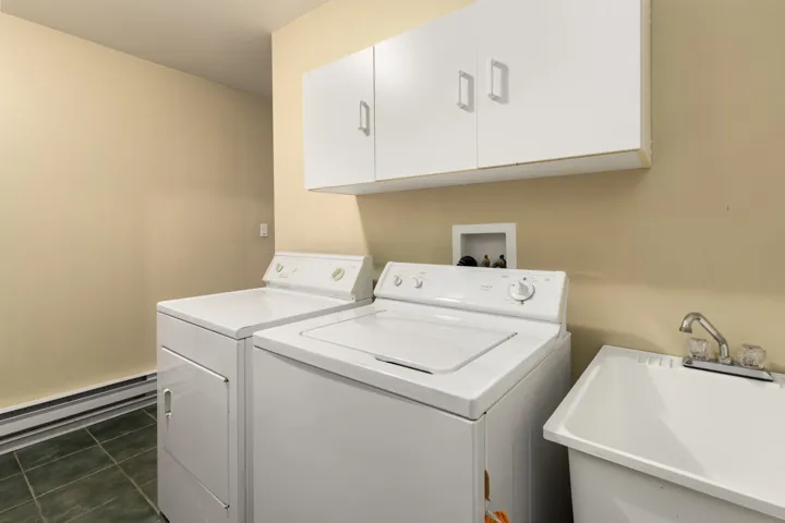 Laundry area featuring a baseboard heating unit, dark tile patterned flooring, independent washer and dryer, second fridge, cabinet space and an entry to the utility room (15'9" x 23'9")