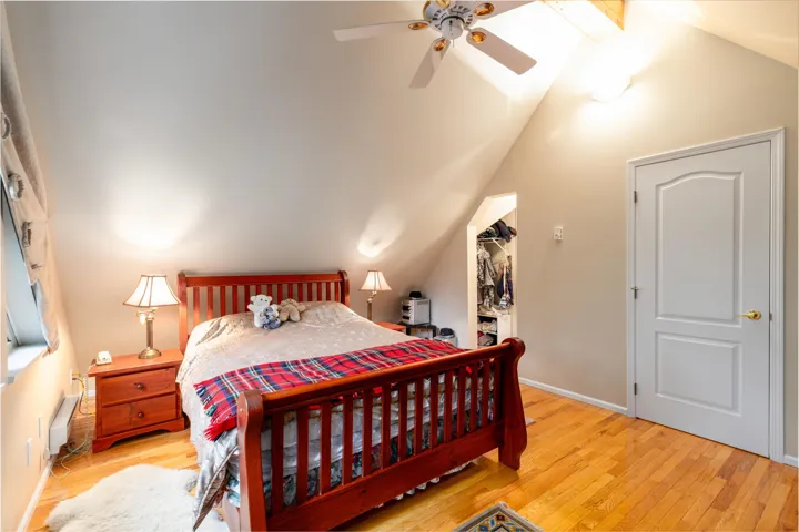 Primary Bedroom with a spacious closet, light wood-type flooring, ceiling fan, beamed ceiling, and a baseboard heating unit