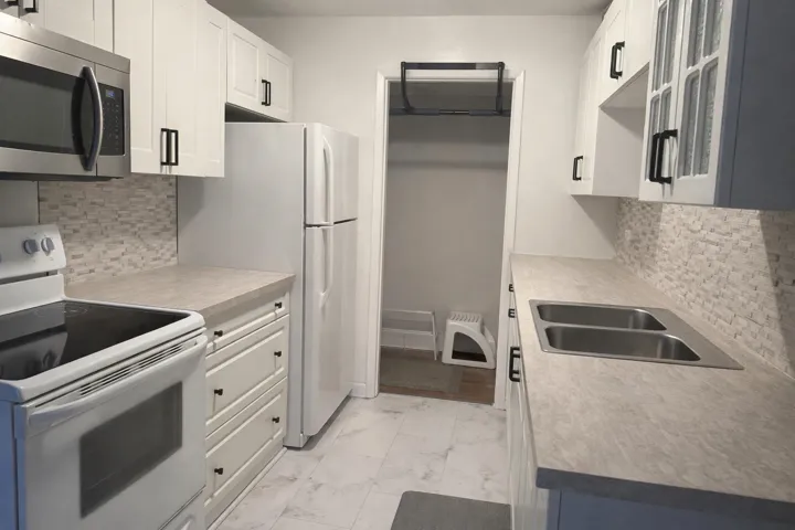 Kitchen featuring electric stove, decorative backsplash, stainless steel microwave, light countertops, and white cabinetry