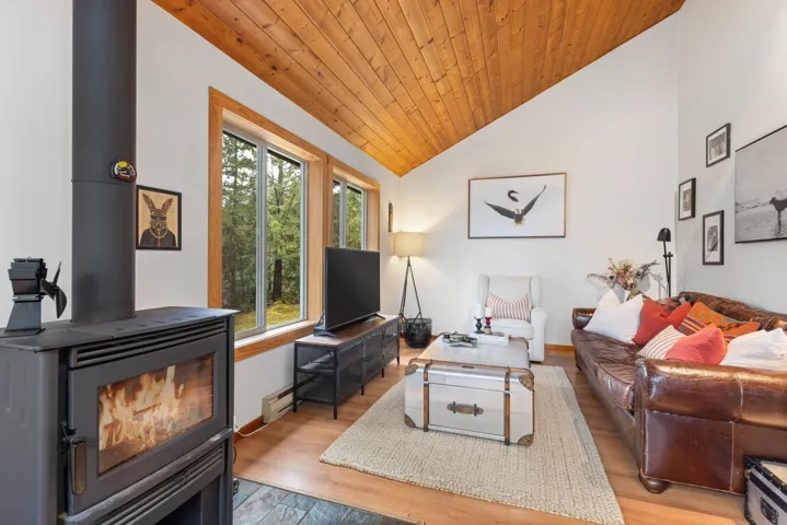 Living area featuring vaulted ceiling, a wood stove, wood ceiling, and light wood finished floors
