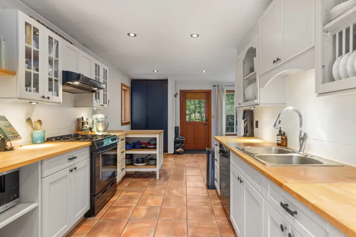 Kitchen featuring black gas range, light tile patterned floors, under cabinet range hood, a sink, and butcher block counters