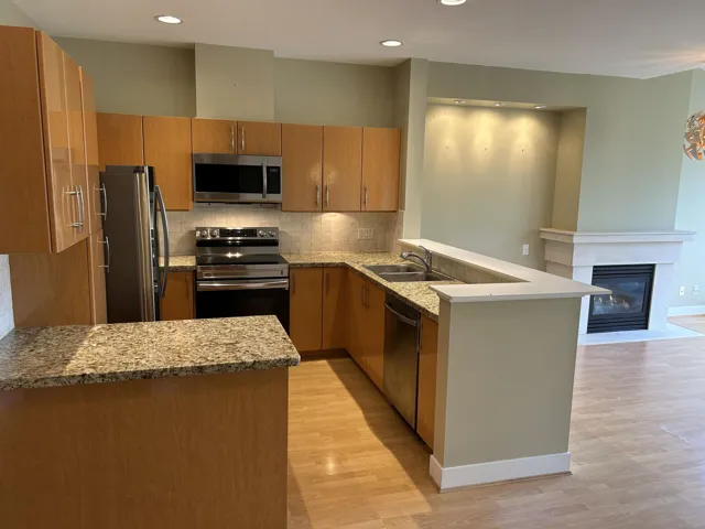 Kitchen with a peninsula, light stone counters, decorative backsplash, appliances with stainless steel finishes. Open floor plan