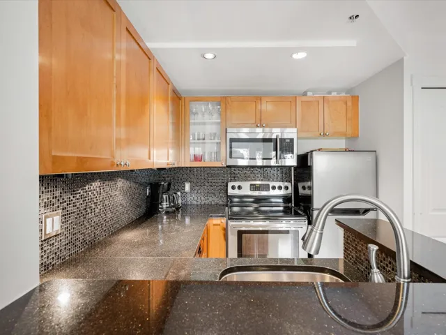 Kitchen with appliances with stainless steel finishes, backsplash, a sink, glass insert cabinets, and dark stone counters