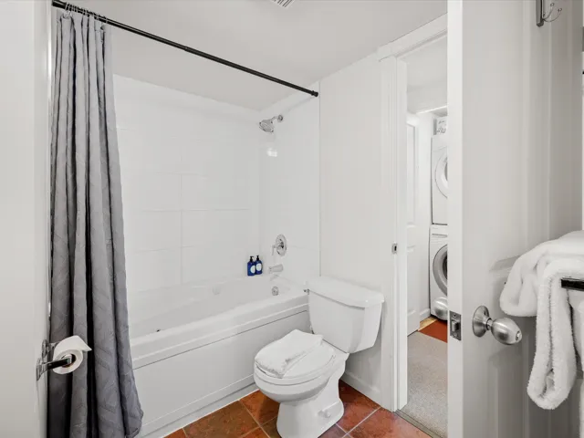 Bathroom featuring stacked washing machine and dryer, shower / bath combo, toilet, and tile patterned floors