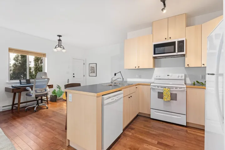 Kitchen with light brown cabinets, a peninsula, white appliances, and a sink