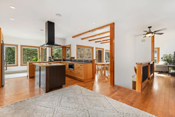 Kitchen featuring beam ceiling, island exhaust hood, light wood finished floors, open floor plan, and a kitchen island