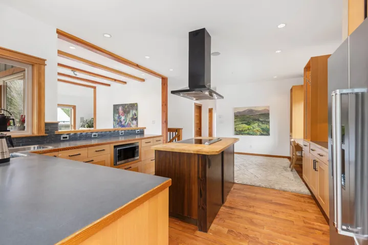 Kitchen with island exhaust hood, built in microwave, black electric cooktop, stainless steel refrigerator with ice dispenser, and wooden counters