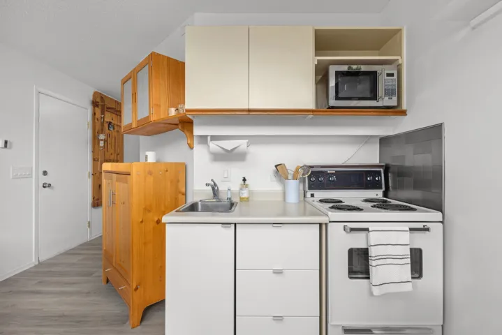 Kitchen with white range with electric stovetop, light countertops, stainless steel microwave, light wood-style flooring, and glass fronted cabinets