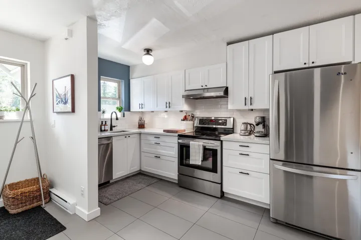 Kitchen with a sink, stainless steel appliances, light countertops, a baseboard heating unit, and under cabinet range hood