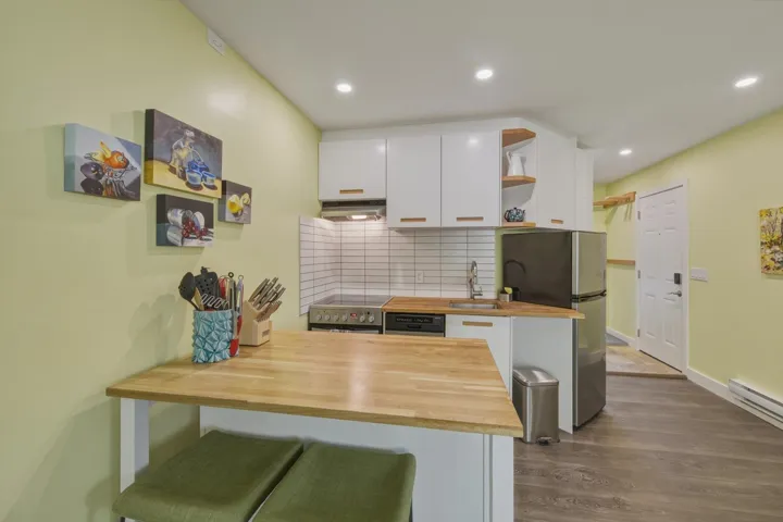 Compact kitchen featuring white cabinetry, light wood-finish countertops, stainless steel appliances, and recessed lighting