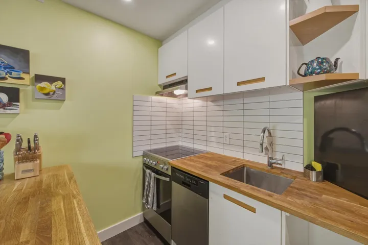 Compact kitchen featuring wood-finish countertops, white shaker cabinetry, stainless steel appliances, and a subway tile backsplash