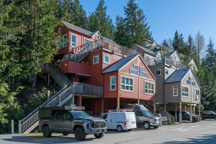Multi-level residential structures featuring red and gray siding, elevated foundations, multiple balconies, extensive exterior staircases, and a natural forested backdrop