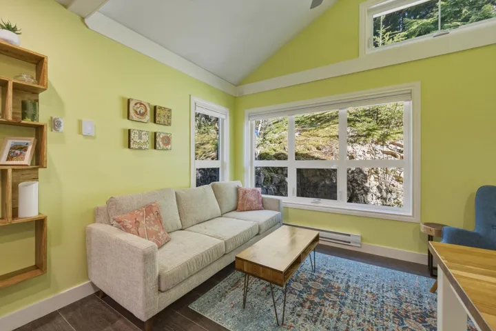 Vaulted ceiling living area featuring wood-finish flooring, a large multi-pane window, and an additional transom window