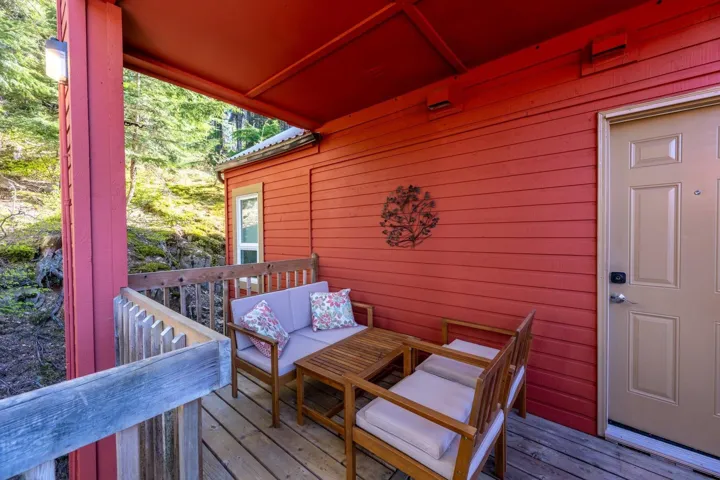 Covered wood deck featuring a vibrant red exterior wall, wood railing, and a side window