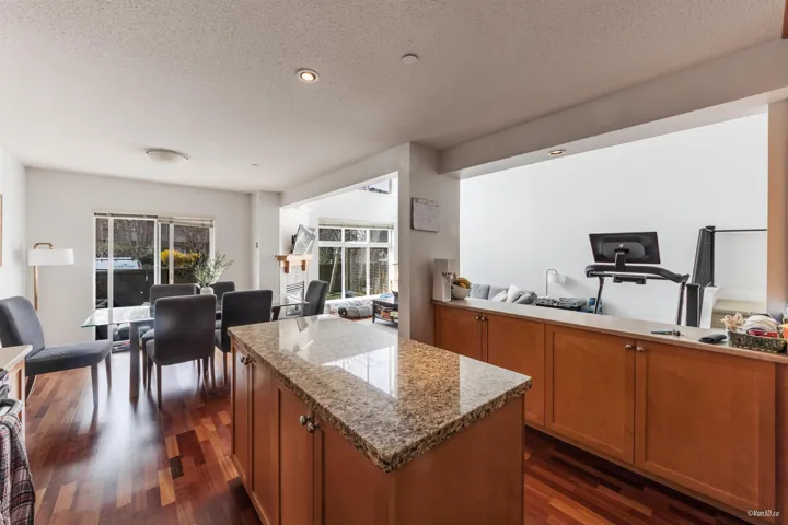 Kitchen featuring brown cabinetry, a kitchen island, light stone counters, dark wood-style flooring, and open floor plan