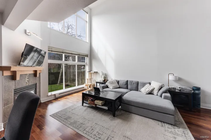 Living room featuring a tiled fireplace, a high ceiling, baseboards, and wood finished floors