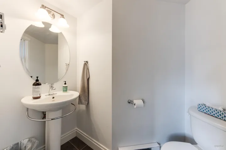 Half bathroom with tile patterned floors, toilet, a baseboard heating unit, and baseboards