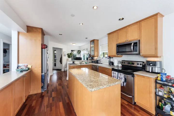 Kitchen with light stone counters, a peninsula, a kitchen island, dark wood finished floors, and appliances with stainless steel finishes