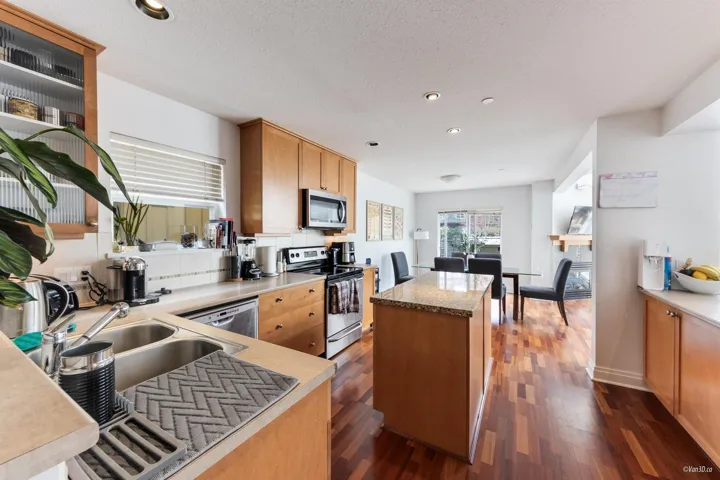 Kitchen with a textured ceiling, a center island, a sink, stainless steel appliances, and dark wood-style floors