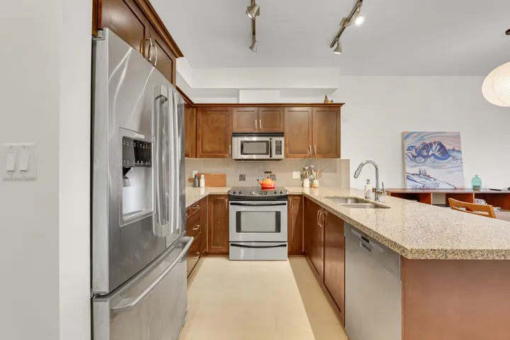 Kitchen featuring a peninsula, tasteful backsplash, appliances with stainless steel finishes, a sink, and light stone counters
