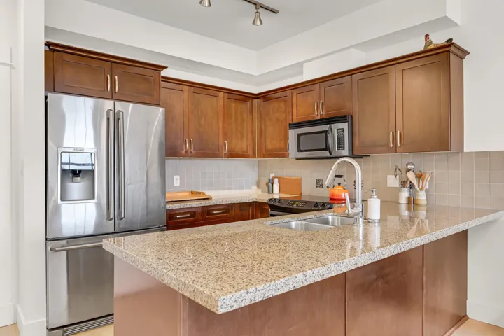 Kitchen featuring light stone counters, backsplash, a peninsula, and appliances with stainless steel finishes
