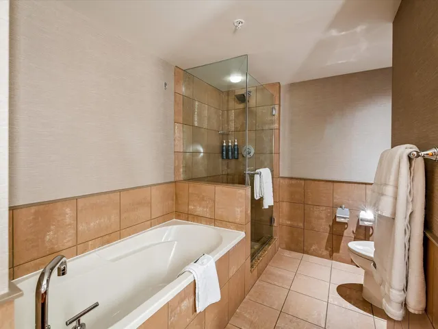 Full bath featuring a bath, tile walls, toilet, tile patterned flooring, and a stall shower