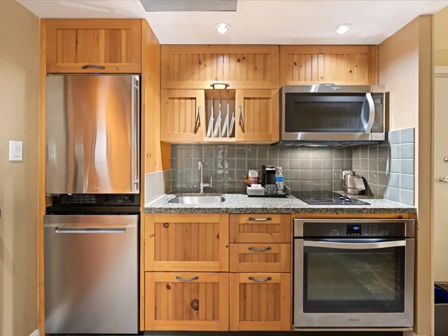 Kitchen with stainless steel appliances, backsplash, light stone counters, and brown cabinets