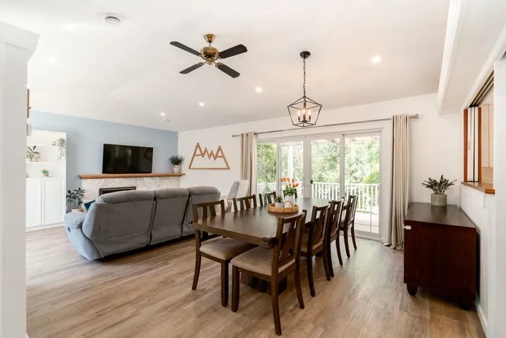 Open-concept living area featuring wood-finish flooring, a stone-faced fireplace with a wood mantle, and a built-in white storage cabinet