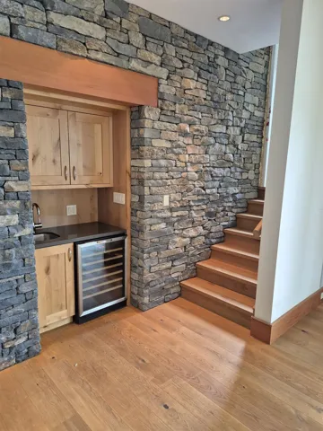 Indoor wet bar with wine cooler, light wood finished floors, light brown cabinets, and dark stone counters
