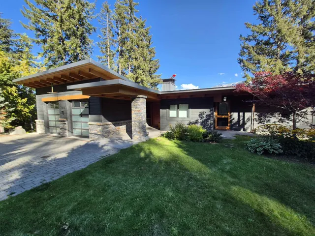 View of front facade with stone siding, a front yard, a chimney, decorative driveway, and a garage