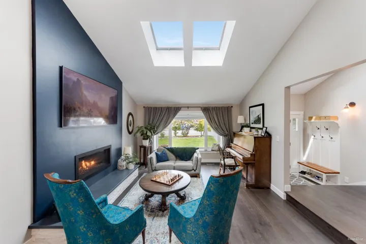 Living room with wood finished floors, a skylight, a glass covered fireplace, baseboards, and high vaulted ceiling