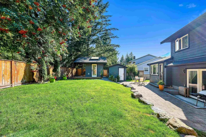 Expansive backyard featuring a large grass area, mature trees, a wooden privacy fence, a paved patio, and two detached sheds