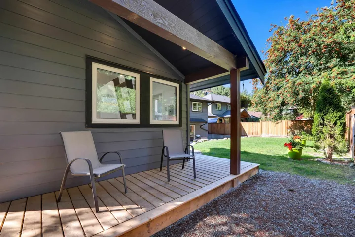 Wood-finish deck with a dark-stained support beam, gray horizontal siding, and white-framed windows