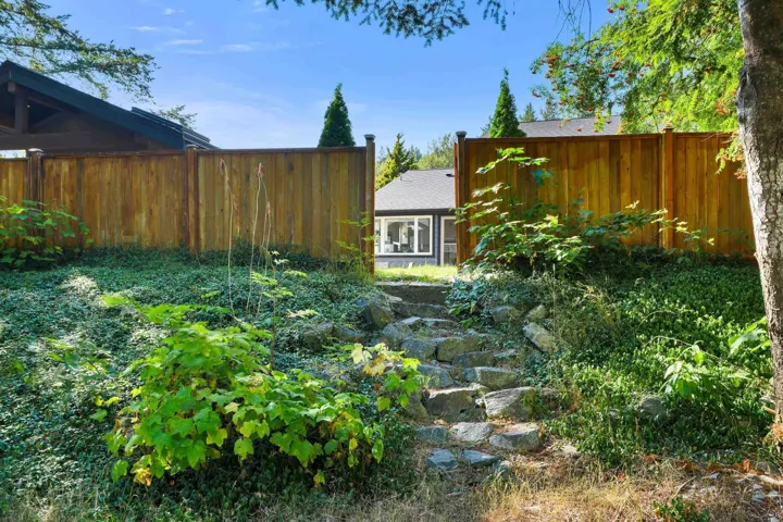 Landscaped backyard featuring natural stone steps, mature trees, and a wooden privacy fence