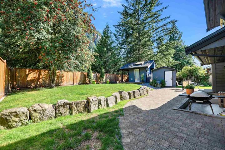 Expansive backyard featuring a manicured lawn, stone retaining wall, private wood fencing, paver patio, and a separate detached outbuilding