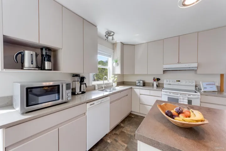 Kitchen featuring white appliances, under cabinet range hood, a sink, stone finish floors, and white cabinets
