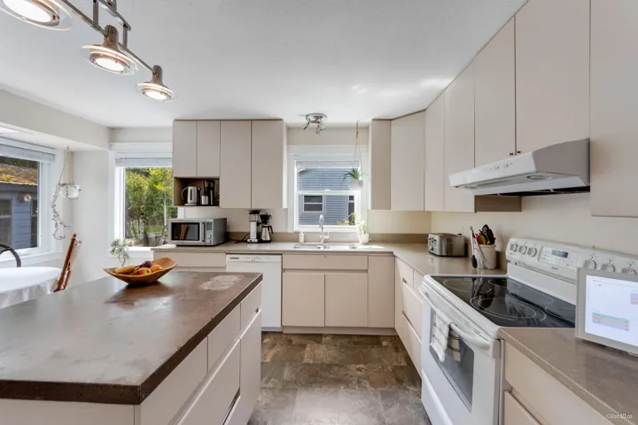 Kitchen with under cabinet range hood, white appliances, a sink, stone finish flooring, and a kitchen island
