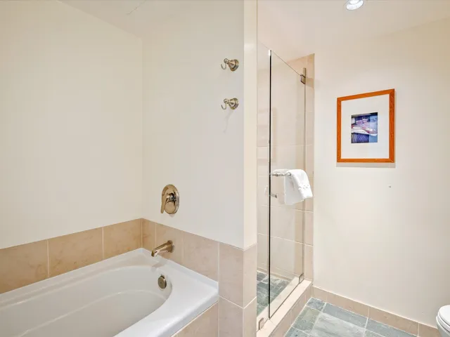 Bathroom featuring toilet, a bath, baseboards, and a stall shower
