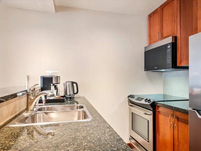 Kitchen featuring tasteful backsplash, a sink, dark countertops, brown cabinets, and stainless steel appliances