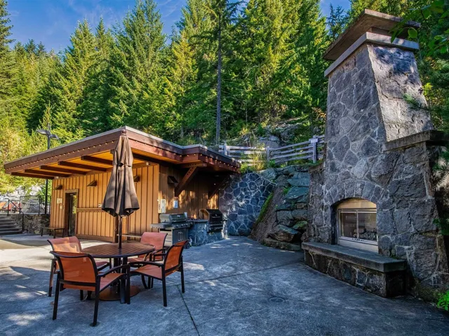 View of patio with an outdoor stone fireplace, area for grilling, a wooded view, exterior kitchen, and outdoor dining area